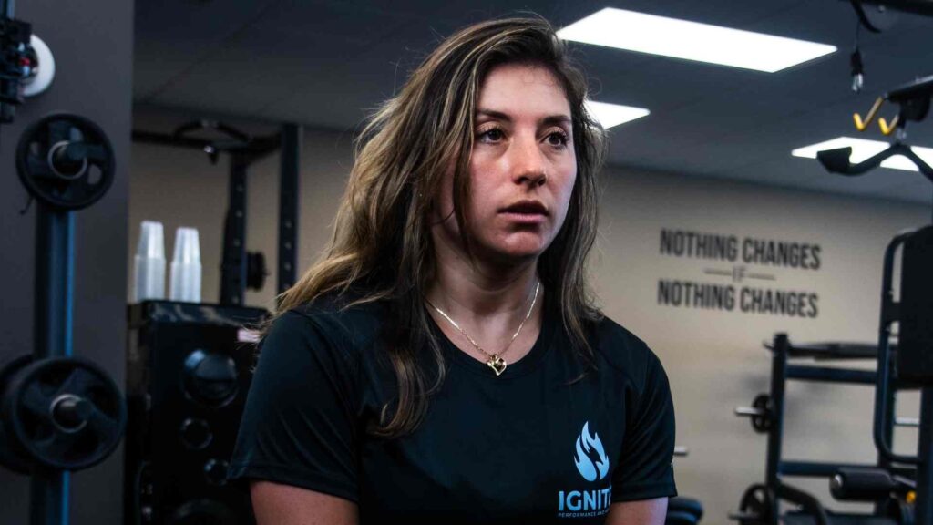 Ignite Performance and Health trainer seated inside the gym near strength-training equipment.
