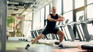 Older man performing a lateral squat exercise in a modern fitness facility.