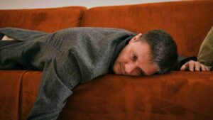 Tired middle-aged man lying face down on a couch and appearing low in energy.