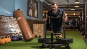 Man pushing a weighted sled during a strength-training workout in a gym.
