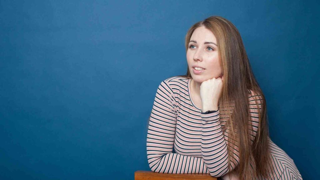 Woman resting her chin on her hand and looking upward against a blue background.