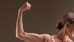 Woman flexing her arm to show muscle development while following a strength-focused health plan.