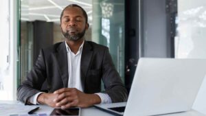 Middle-aged man sitting at a desk with his eyes closed, taking a quiet pause during the workday.