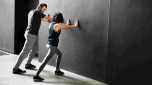 Personal trainer guiding a woman through a wall-supported exercise during a fitness session.