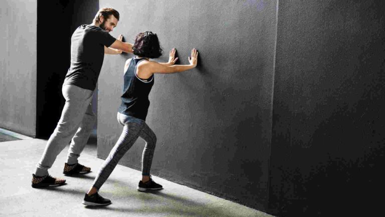 Personal trainer guiding a woman through a wall-supported exercise during a fitness session.