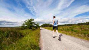 Man running along a rural road under a bright blue sky.