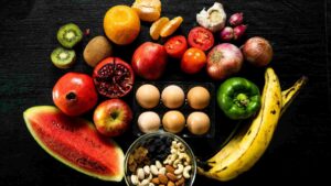 Assortment of fruits, vegetables, eggs, and nuts arranged on a dark surface.