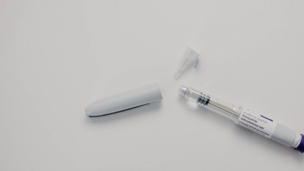 Tirzepatide injection pen and needle cap on a white surface.