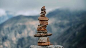 Stack of balanced stones overlooking mountains, representing progress, resilience, and lasting transformation.
