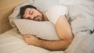 Man sleeping comfortably in bed, representing rest, recovery, and physical performance.
