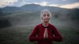 Older woman practicing mindful breathing outdoors with mountains in the background.