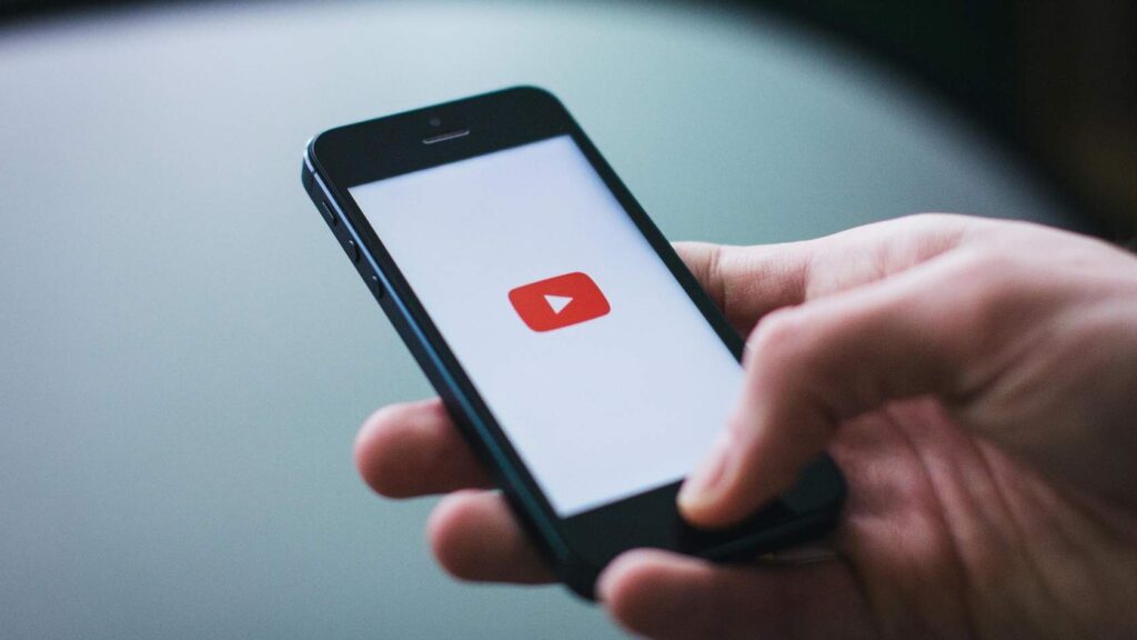 Person holding a smartphone with a video play icon on the screen, representing Ignite educational videos.