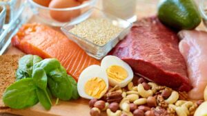 Protein-rich foods including salmon, lean beef, chicken, eggs, quinoa, nuts, spinach, and avocado.
